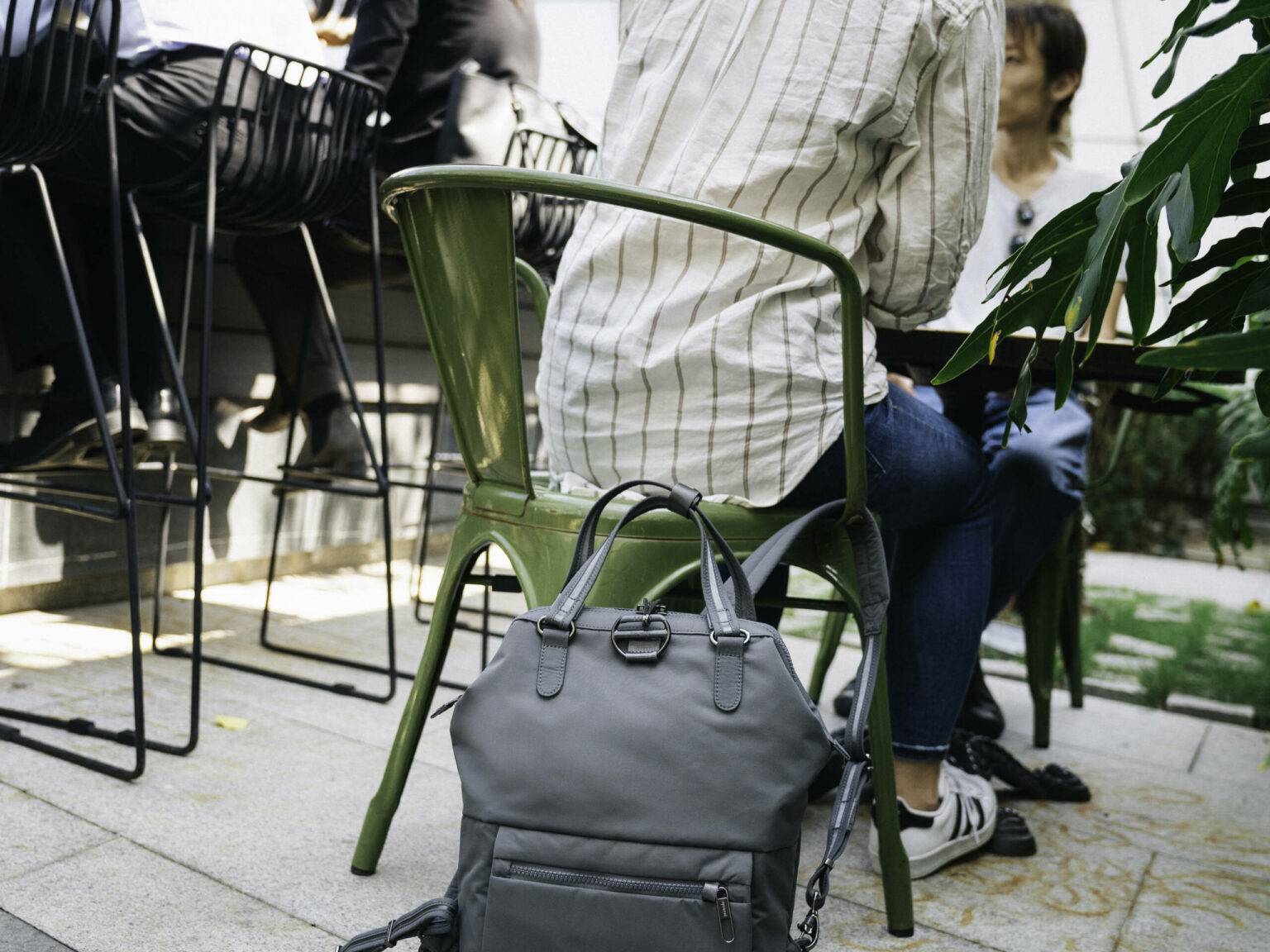 Eine Reisende kann dank des nützlichen Reise-Gadgets von Pacsafe ihren Rucksack am Stuhl befestiegen.