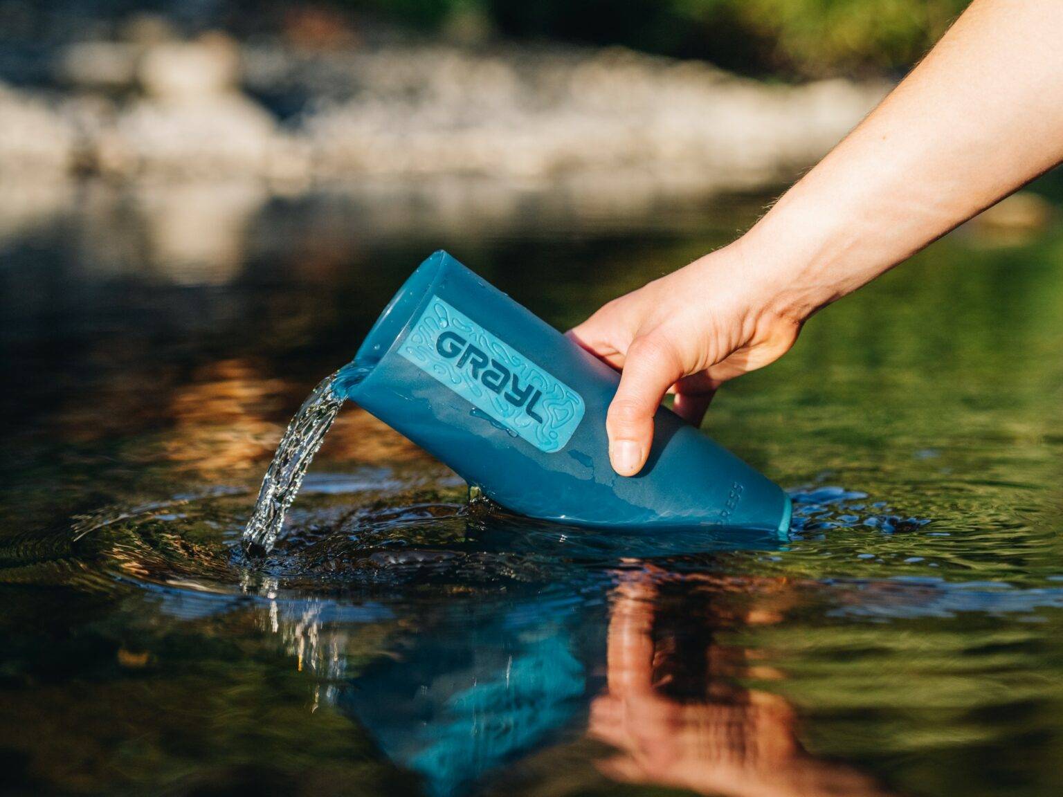 In natürlichem Gewässer lässt sich mit dem praktischen Wasserfilter von Grayl Wasser auf Reisen filtern.