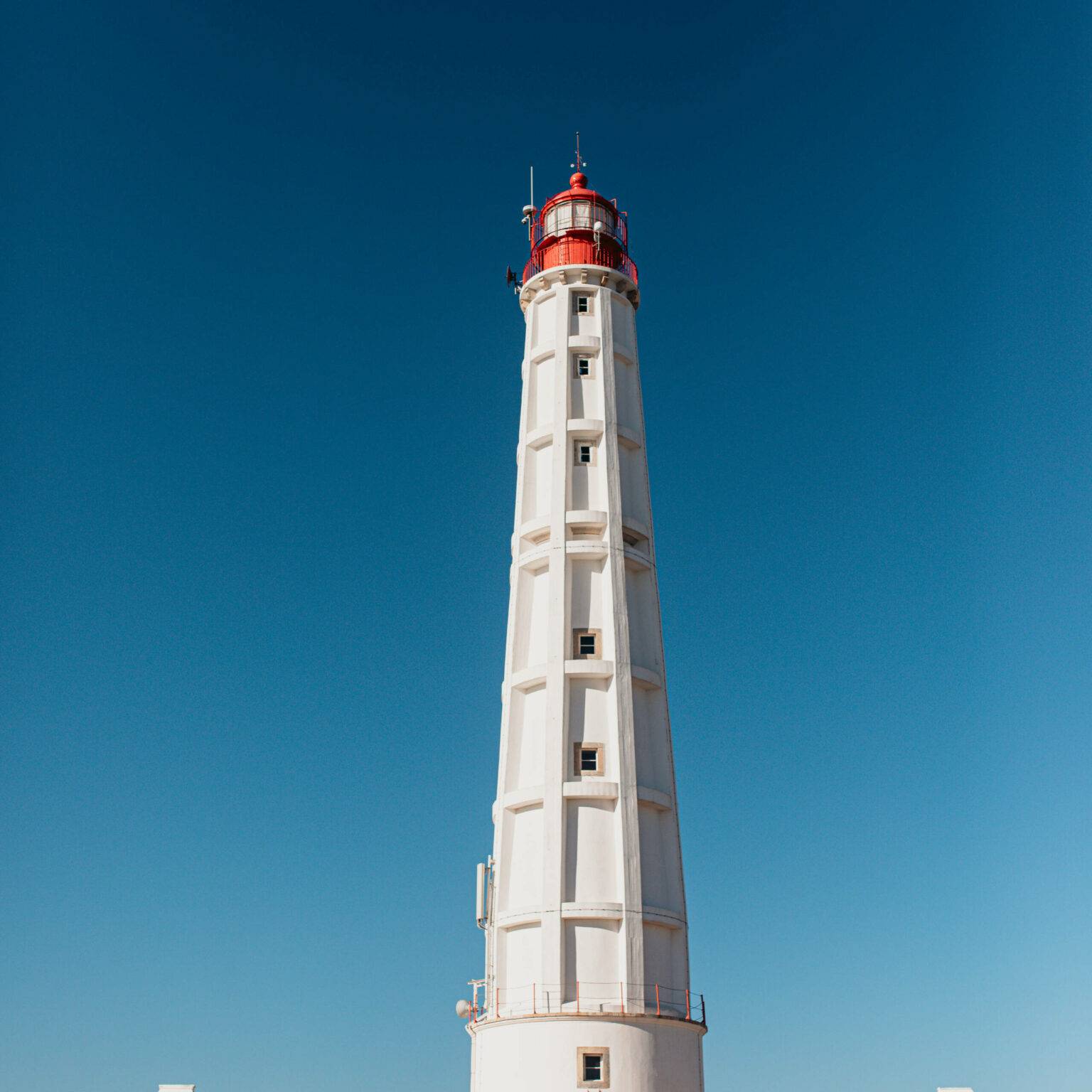 Der weiße Leuchtturm mit dem roten Dach ragt auf der Ilha do Farol in den strahlend blauen Himmel.